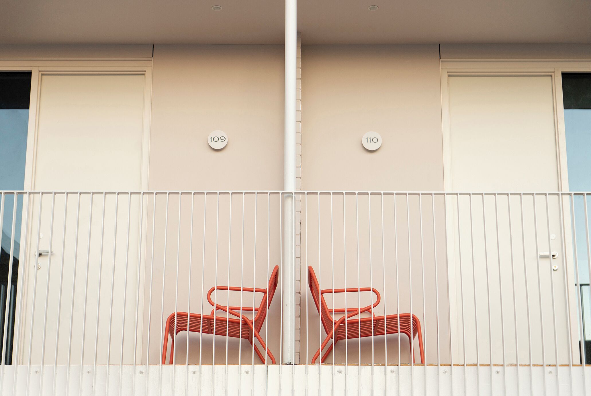 A balcony with two red chairs, white railings, and doors numbered 109 and 110.