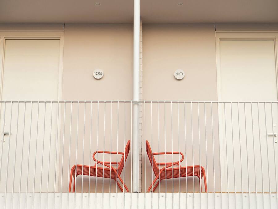 A balcony with two red chairs, white railings, and doors numbered 109 and 110.