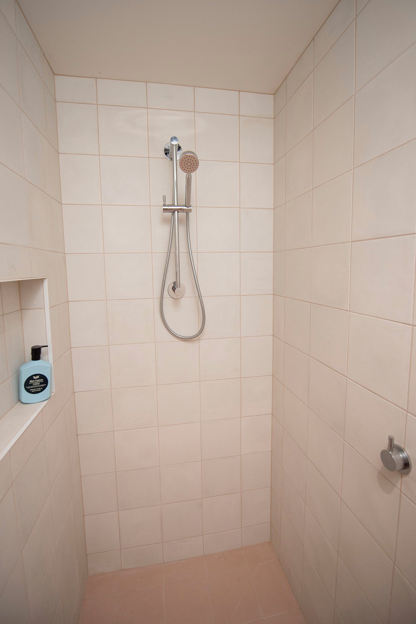 A small, tiled shower room with a handheld showerhead and a wall-mounted faucet.