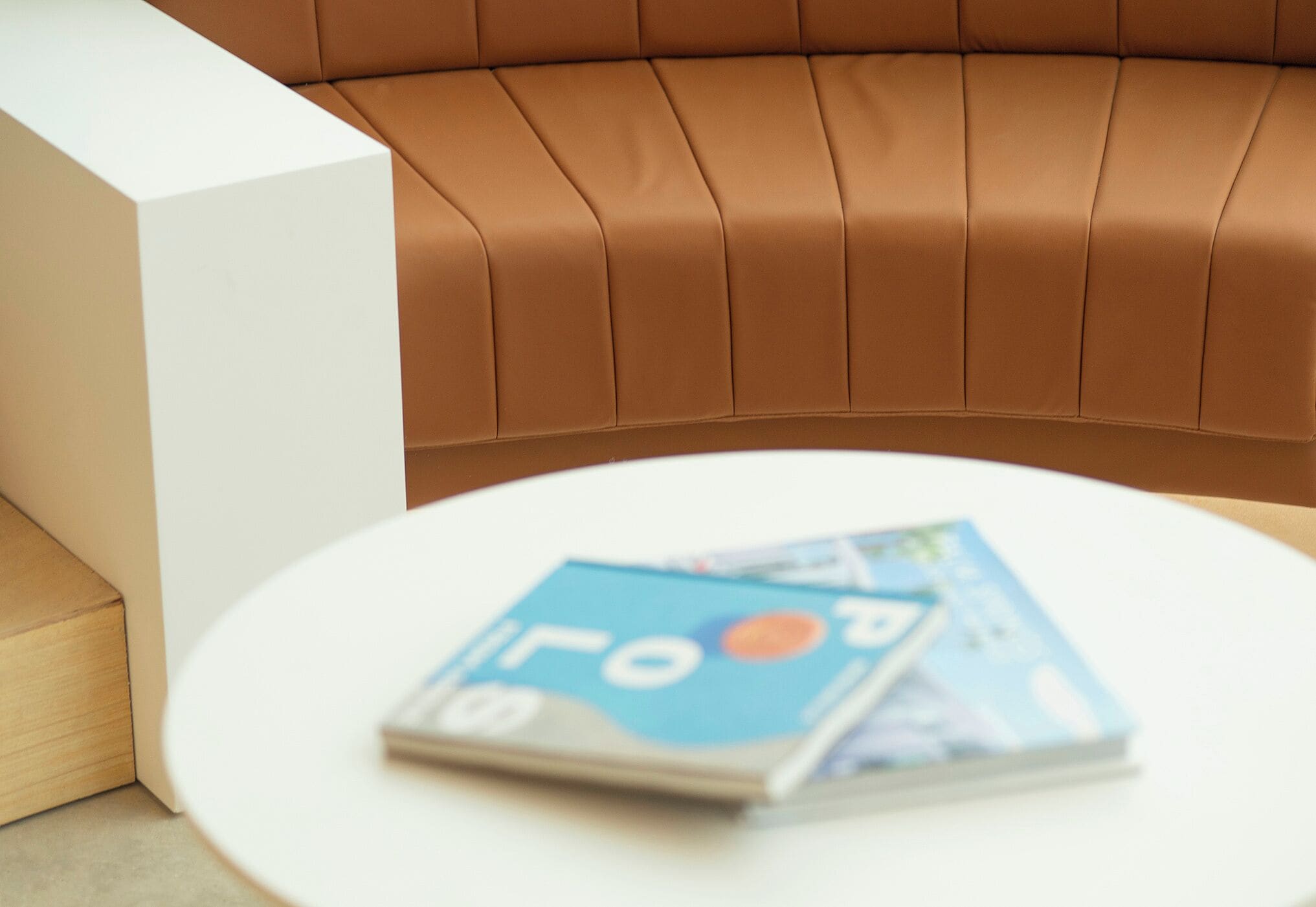 A magazine on a white table next to a brown leather couch.