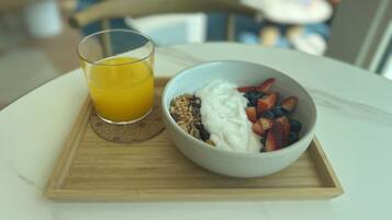 Bandeja de desayuno con vaso de jugo de naranja y tazón de yogur con frutos rojos sobre tabla de madera.