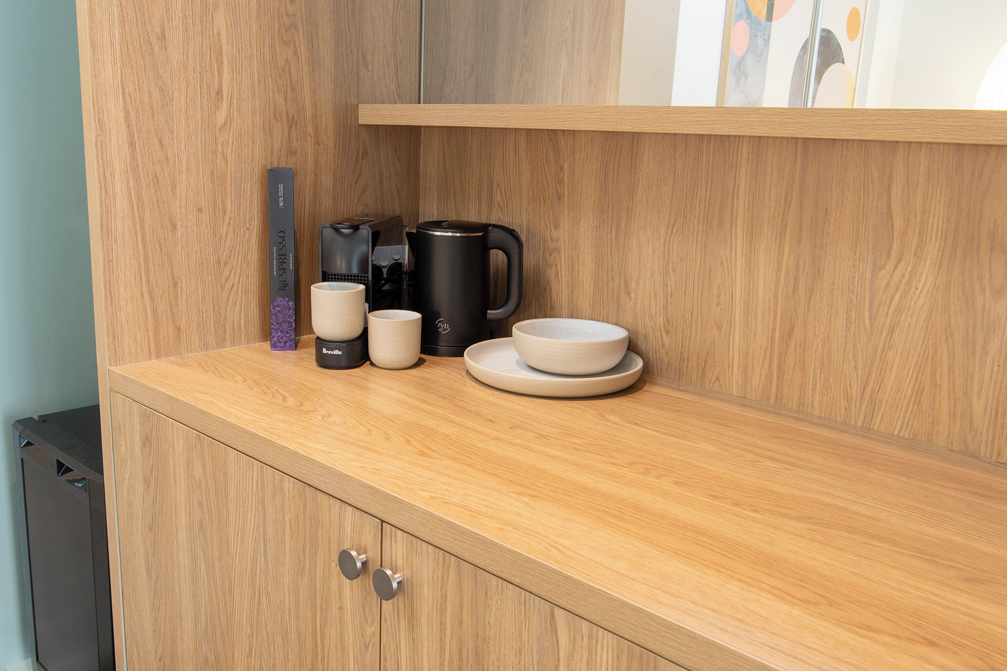 A wooden countertop with a coffee maker, cups, and a box.