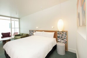 A hotel room with a large bed, a green armchair, a small table, and a lamp.