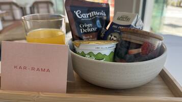 A breakfast tray with a glass of orange juice, a packet of Carmun's Crispy Deluxe, a container of milk, and a bowl with strawberries and yogurt.