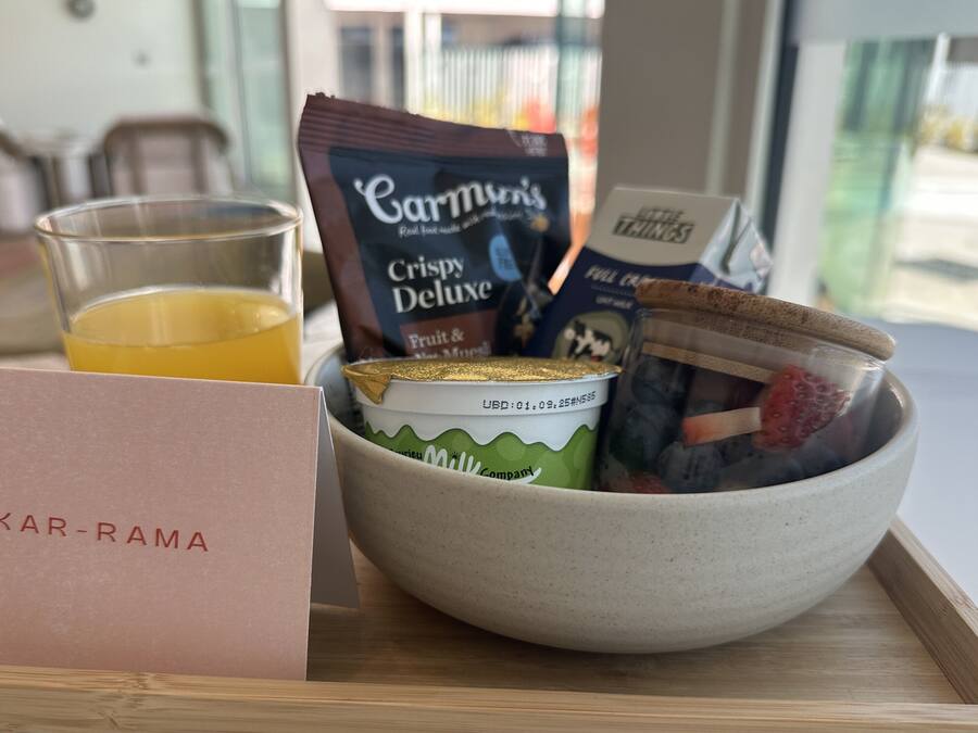 A breakfast tray with a glass of orange juice, a packet of Carmun's Crispy Deluxe, a container of milk, and a bowl with strawberries and yogurt.