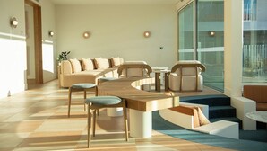 A modern living room with a curved wooden coffee table, a sofa set, and a large window offering a view of the city. - Kar-Rama Hotel  (Mildura)