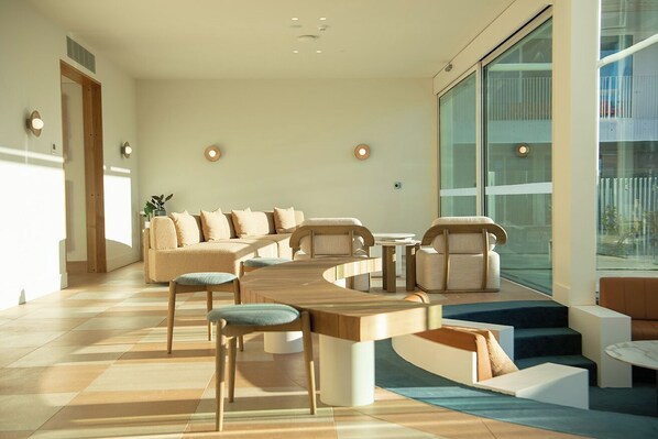 A modern living room with a curved wooden coffee table, a sofa set, and a large window offering a view of the city.