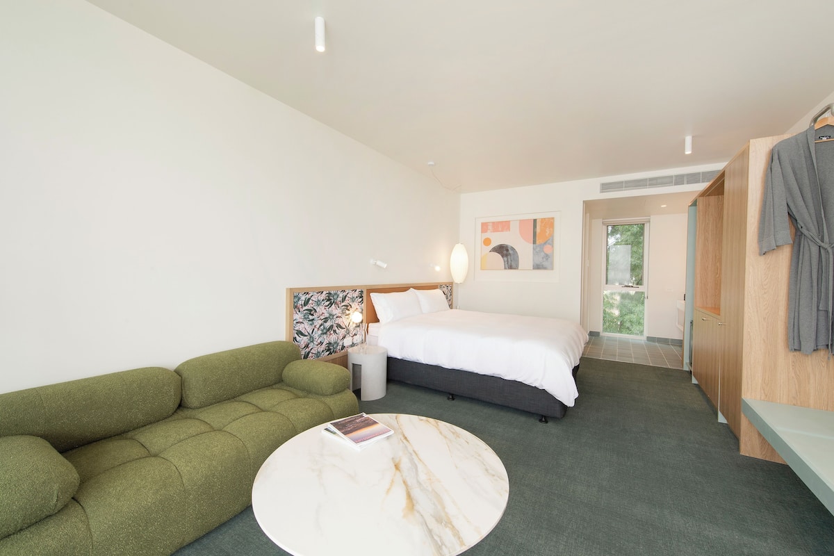 A hotel room with a bed, a green sofa, a round table, and a wooden wardrobe.