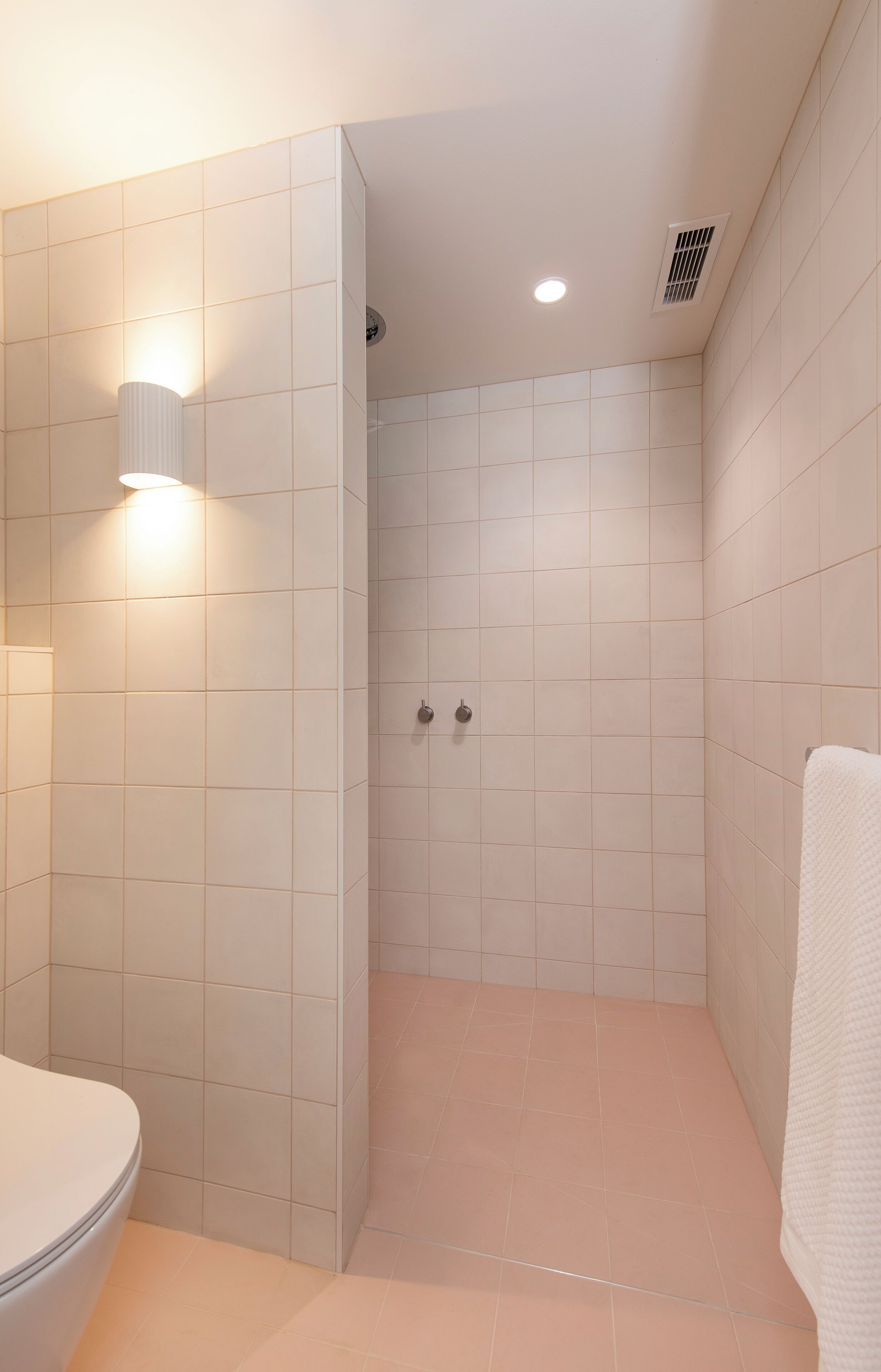 Un baño moderno con azulejos blancos, un inodoro, una zona de ducha y un perchero para toallas.