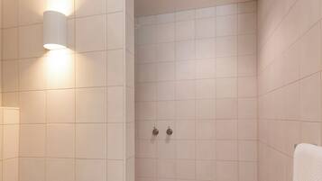 Un baño moderno con azulejos blancos, un inodoro, una zona de ducha y un perchero para toallas.