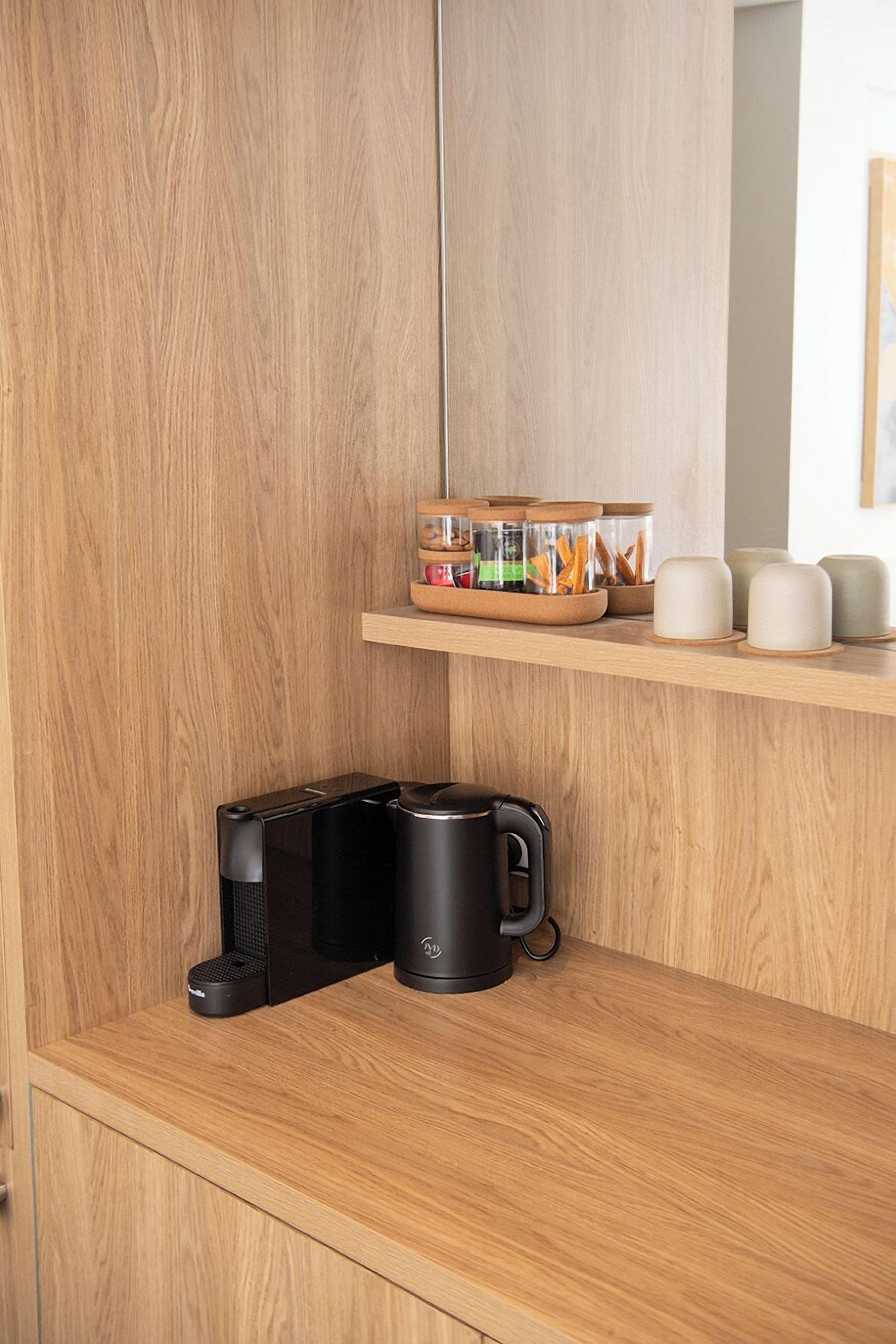 A kitchen area with wooden cabinets, a countertop, and a shelf with jars and mugs.