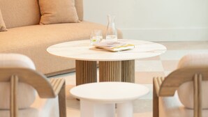 A modern living room with a beige sofa, a round coffee table with a book and glasses, and two chairs. - Kar-Rama Hotel  (Mildura)