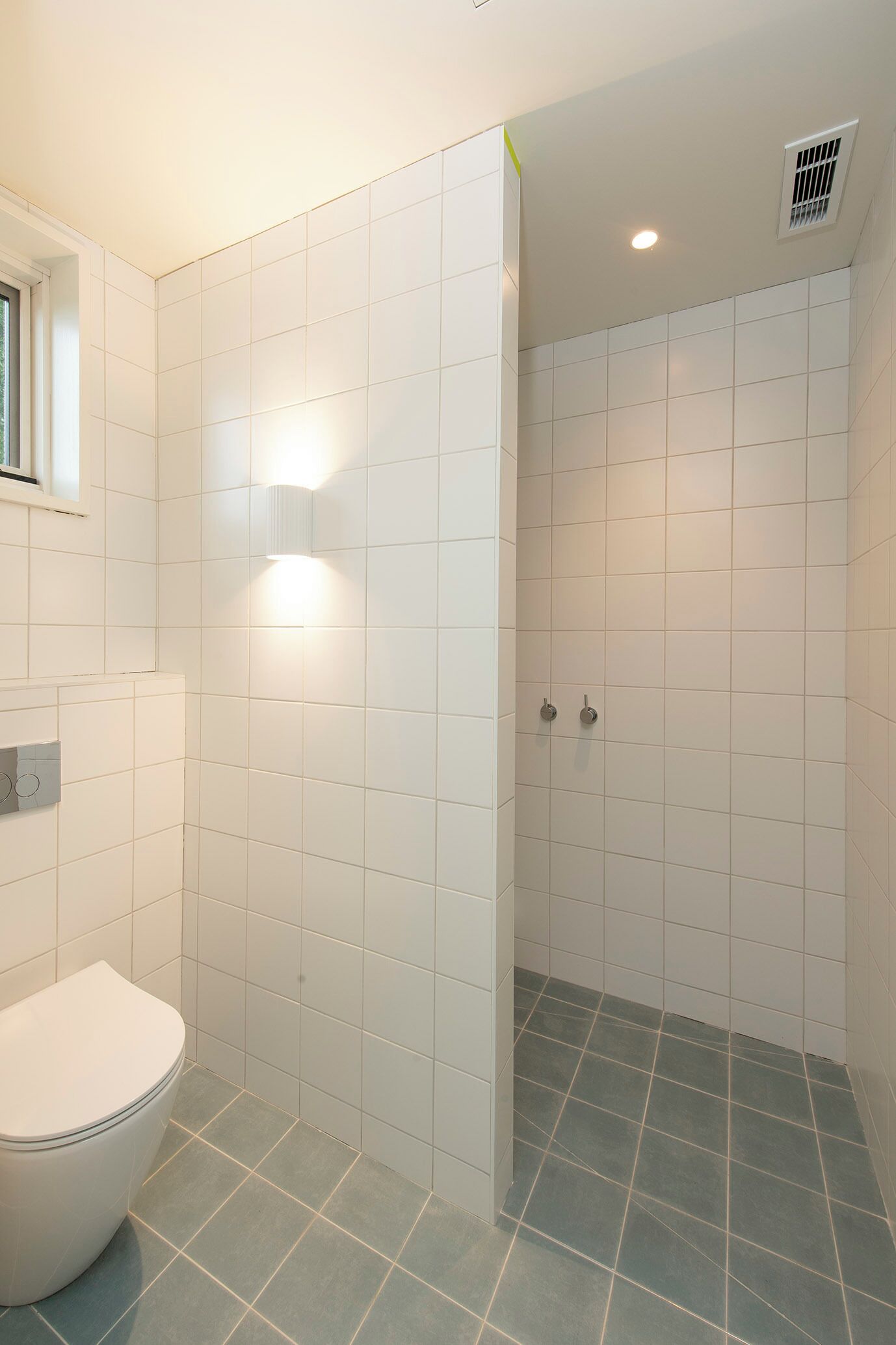 Une salle de bain avec des carreaux blancs, des toilettes et un espace douche.