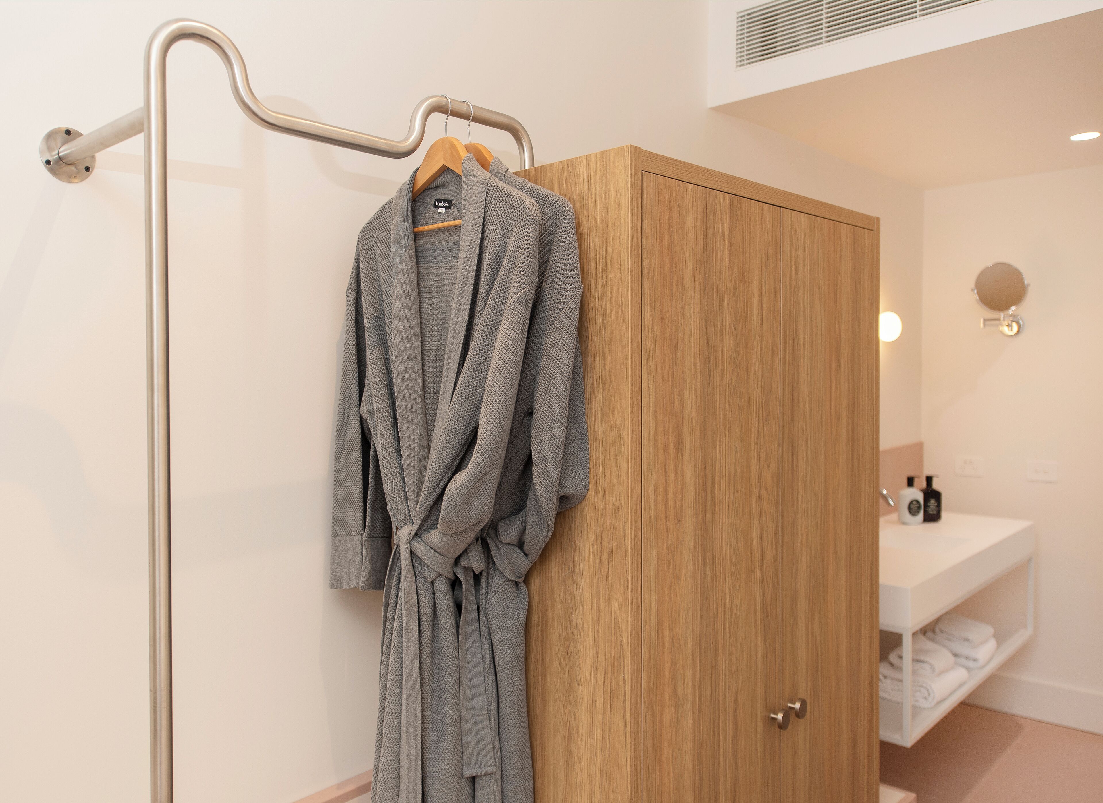 A bathroom with a wooden wardrobe, a towel rack, and a sink with toiletries.