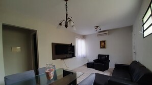 Una sala de estar con televisor, sofá, una mesa de centro de vidrio y una araña.