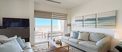 Un salón moderno con sofá, mesa de centro y televisión. Tiene un balcón con vistas.