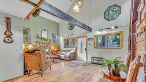 A spacious living room with a fireplace, wooden beams, and large windows.