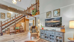 A spacious living area with a wooden staircase, a large painting, and a dining table.