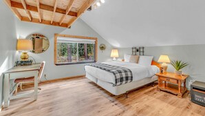 A bedroom with a bed, bedside tables, a desk, and a window with a view of trees.