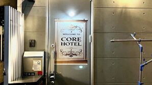 A hotel entrance with a 'Welcome to Core Hotel' sign, a security keypad, and a metal door. - COREHOTEL (Tokyo)