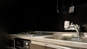A modern kitchen with stainless steel appliances, a sink, and hanging utensils. - COREHOTEL (Tokyo)