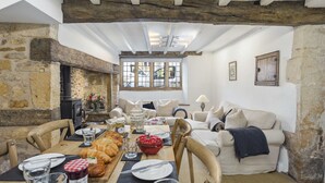 Un comedor rústico con paredes de piedra, una mesa de madera dispuesta para una comida y un espacio de sala acogedor con un sofá y una lámpara.