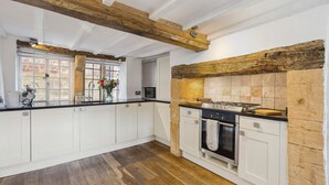 Una cocina con armarios blancos, piso de madera, pared de ladrillo y un ventanal grande.