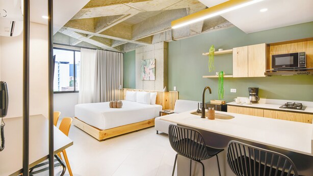 A modern hotel room with a bed, a desk, a kitchenette, and a bathroom. - Firenze Lofts (Medellín)