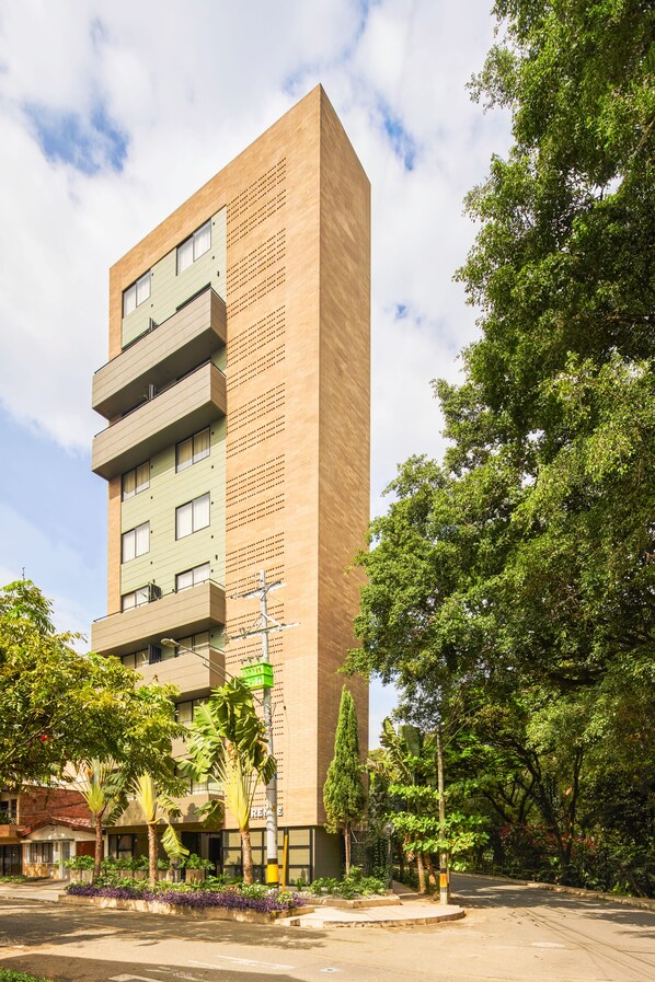 A modern building with multiple floors, balconies, and a landscaped area with trees and plants. - Firenze Lofts (Medellín)