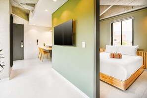 A modern hotel room with a large bed, a flat-screen TV, a desk with chairs, and a window with a city view. - Firenze Lofts (Medellín)