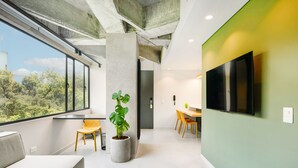 A modern interior with a large window, a potted plant, a sofa, a dining area, and a flat-screen TV. - Firenze Lofts (Medellín)