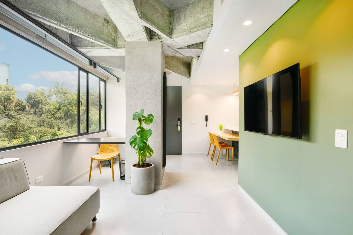 Un interior moderno con un amplio ventanal, una planta en maceta, un sofá, un comedor y un televisor de pantalla plana.