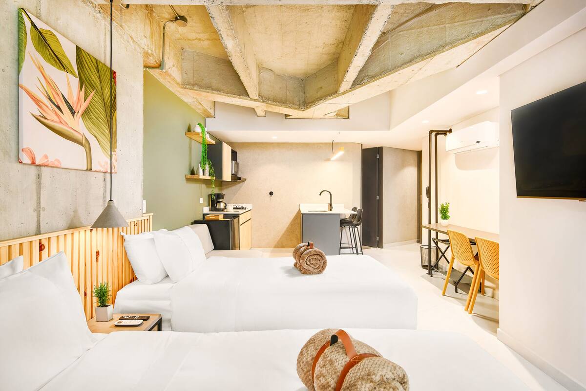 Una habitación de hotel moderna con una cama grande, un escritorio, una silla y una pequeña cocina.