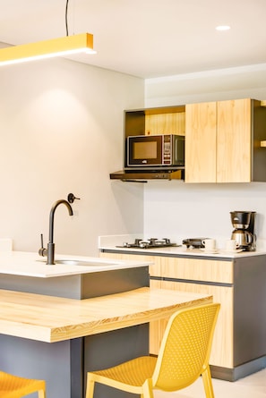 A modern kitchen with a central island, a microwave above the counter, and a coffee maker on the countertop. - Firenze Lofts (Medellín)