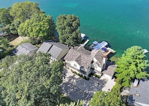 An aerial view of a house with a large deck overlooking a body of water, surrounded by trees.