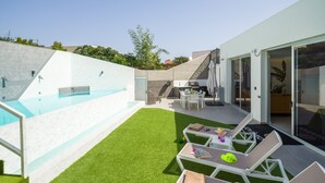 A modern outdoor pool area with a small patio and lounge chairs.