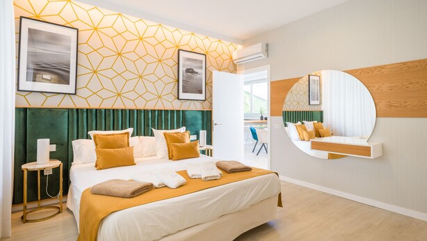 A modern hotel room with a large bed, a bedside table, a mirror, and geometric wall decor.