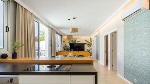 A modern kitchen with a built-in stove, white cabinetry, and a dining area with a yellow sofa and a TV.