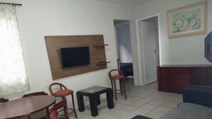 A living room with a TV mounted on the wall, a dining table with chairs, a sofa, and a cabinet. - Round trip - LA11-Bertioga, SESC, Riviera, Vista Linda, Indaiá (Jardim Rafael Bertioga)