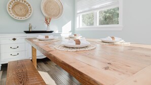 Een eetgedeelte met een houten tafel, witte kasten en twee wanddecoraties van geweven materiaal.