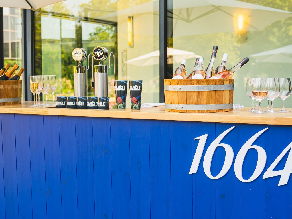 A bar area with a blue counter, numbered 1664, featuring a wine bottle holder, glasses, and branded beer taps.