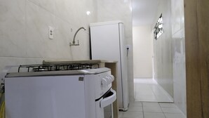 Une cuisine compacte avec des appareils électroménagers blancs, notamment une cuisinière à gaz et un réfrigérateur, dans un appartement moderne.