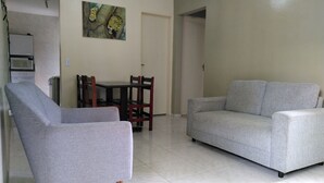 Un salon avec un canapé gris, un fauteuil gris, une table à manger avec des chaises et un tableau accroché au mur.