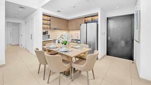 Une cuisine moderne dotée d’appareils électroménagers intégrés, un coin repas avec une table dressée pour quatre personnes, et une grande porte noire.
