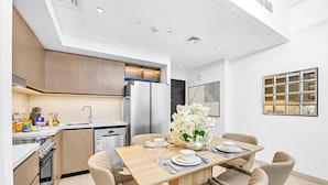 Une cuisine moderne avec un coin repas, comprenant une table en bois dressée pour quatre personnes, un réfrigérateur et un lave-vaisselle.