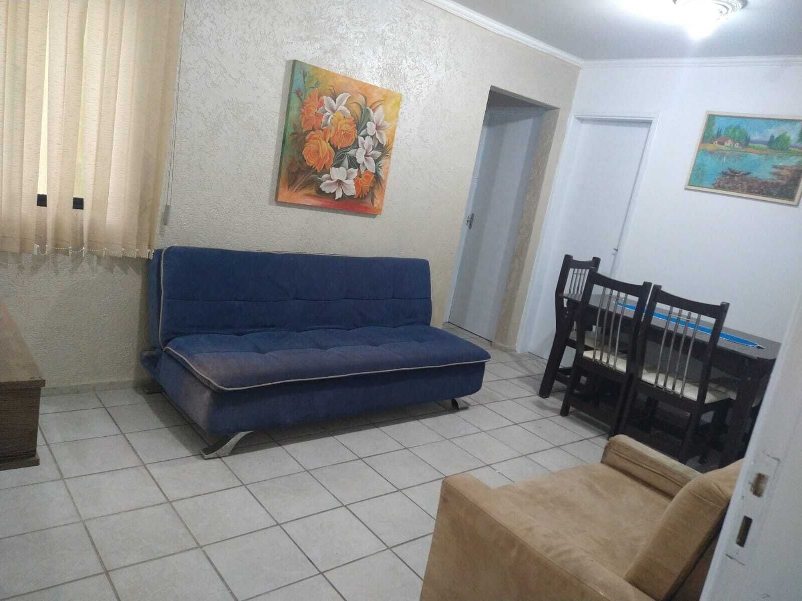 Una sala de estar con un sofá azul, una mesa de comedor con sillas y dos cuadros en las paredes.