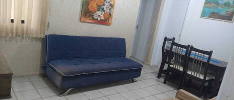 Una sala de estar con un sofá azul, una mesa de comedor con sillas y dos cuadros en las paredes.