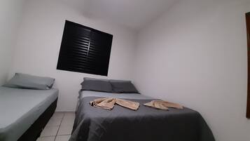 Um quarto pequeno e compacto com uma cama de solteiro, uma cama menor e uma janela com persianas.