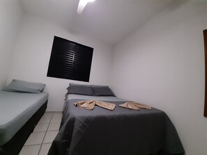 A small, compact bedroom with a single bed, a smaller bed, and a window with blinds.