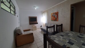 Un salon comprenant un canapé, un téléviseur fixé au mur, une table à manger avec des chaises et un tableau accroché au mur.